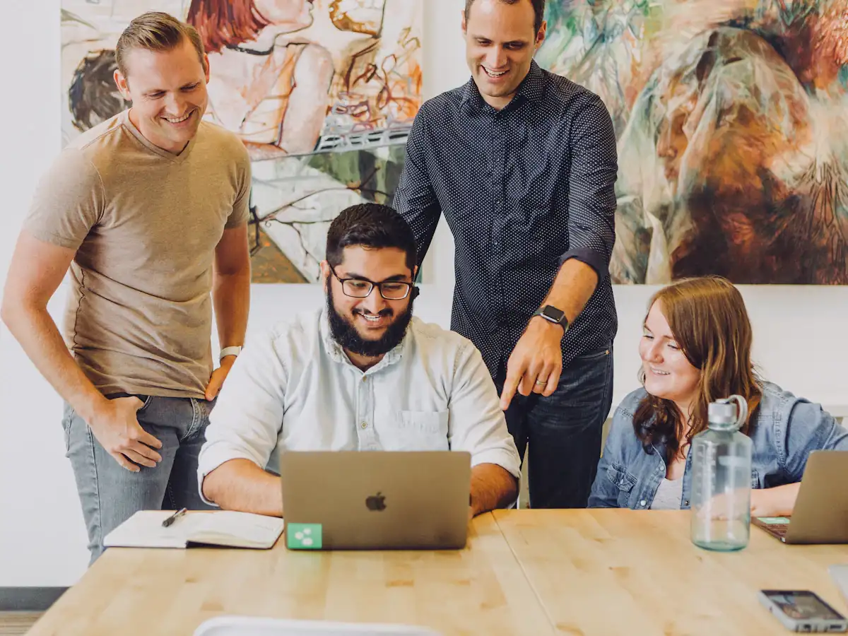 Four coworkers smiling around a laptop at a table