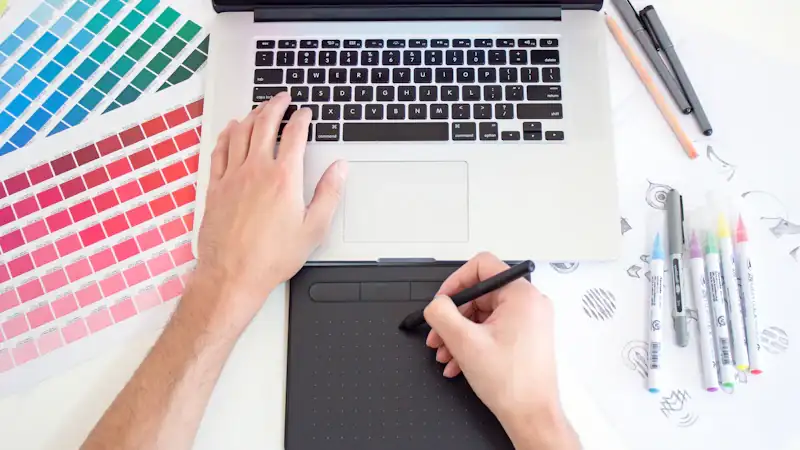 Designer using a drawing tablet and laptop with colour swatches
