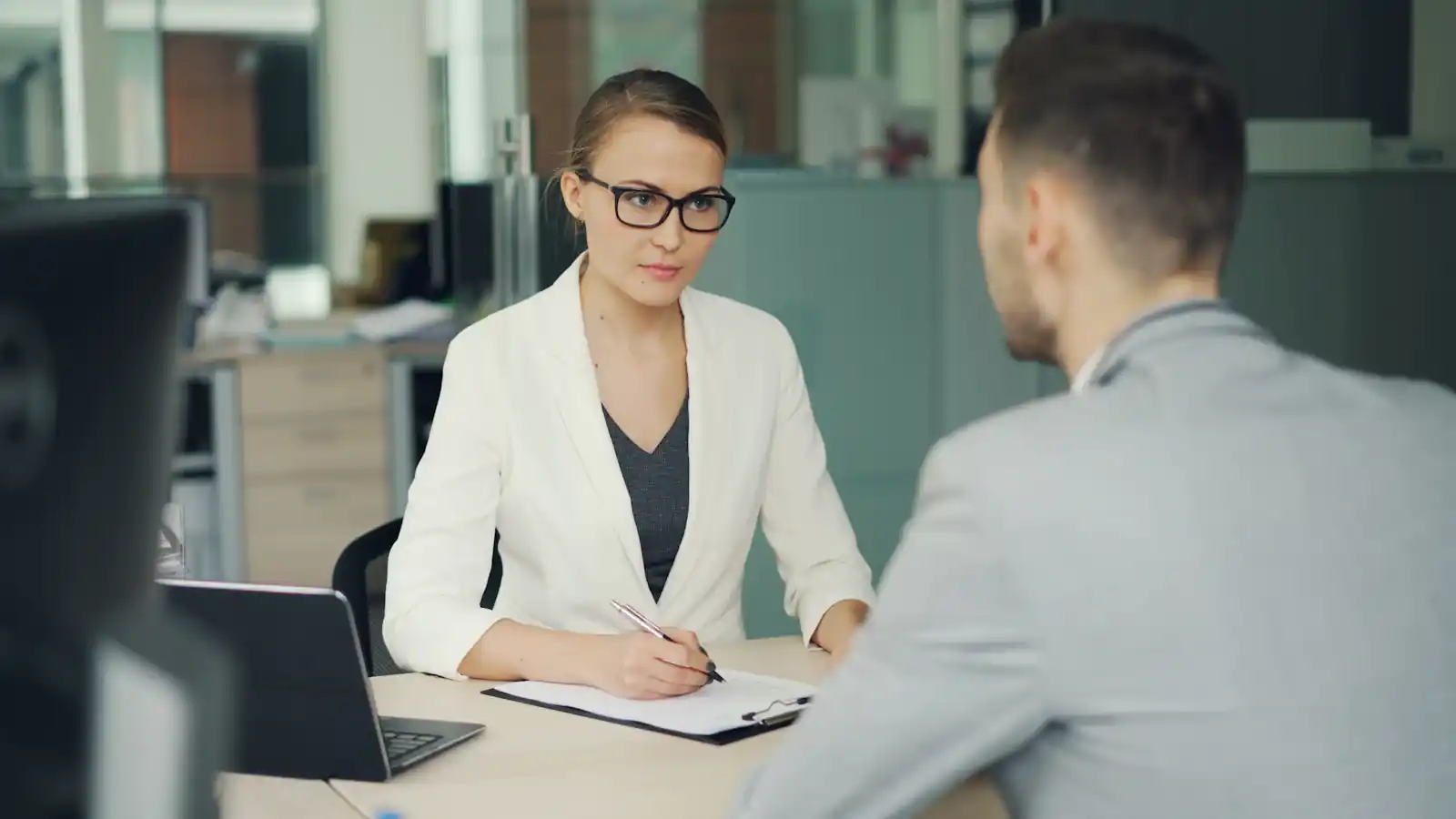 Recruiter in glasses interviewing a candidate across an office desk