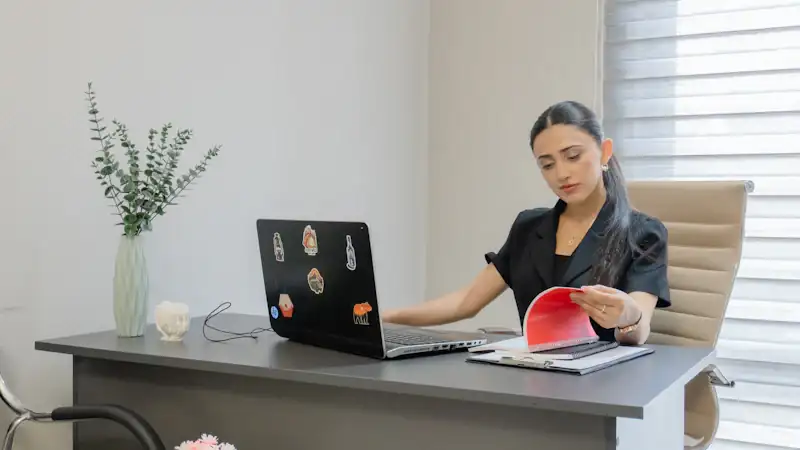 Woman working on a laptop while reading papers at a desk