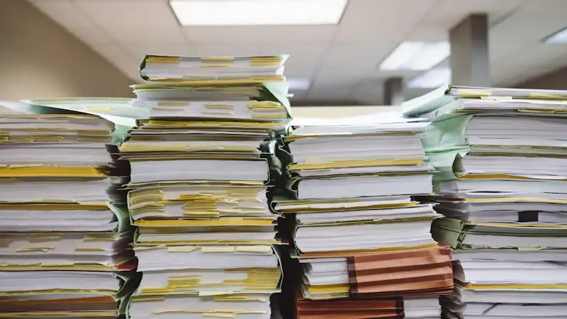 Stacks of paper documents and file folders on a desk