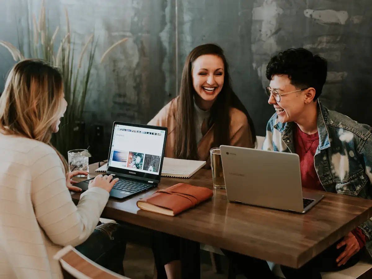 Three colleagues laughing together while working on laptops